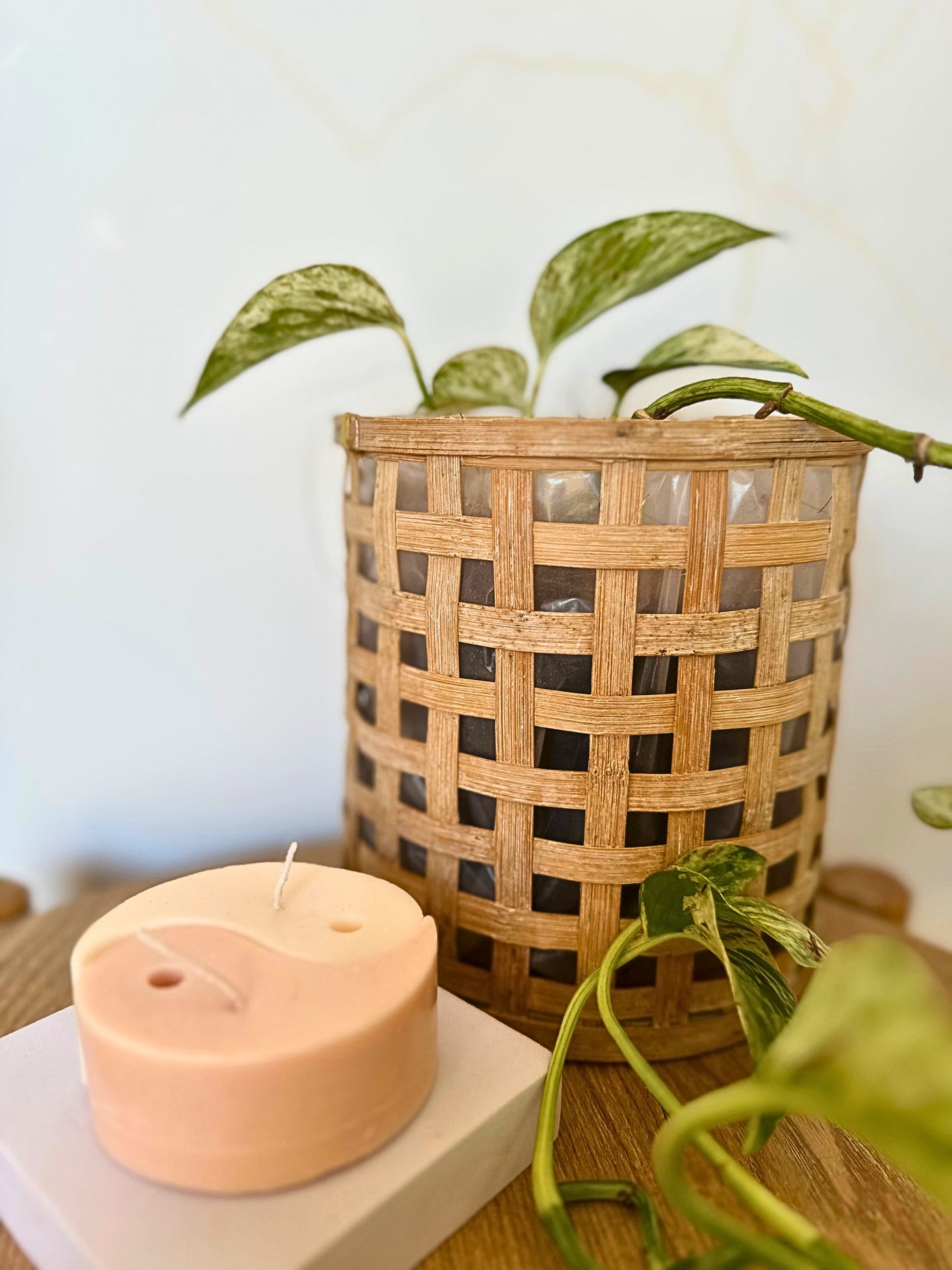 Heart-shaped candle on a white surface with a woven basket and plant in the background.
