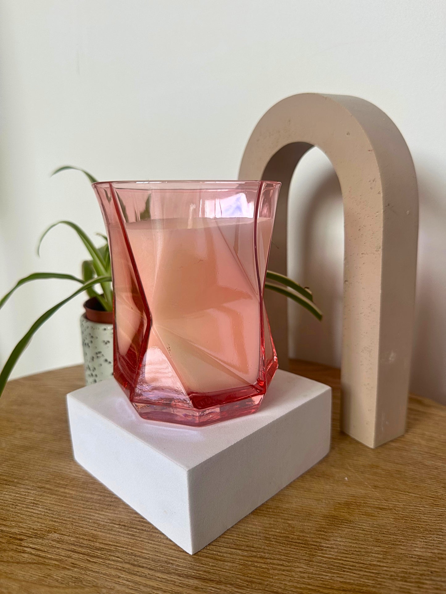 Pink Hikari Candle in Pink on a white pedestal with a plant and arch in the background
