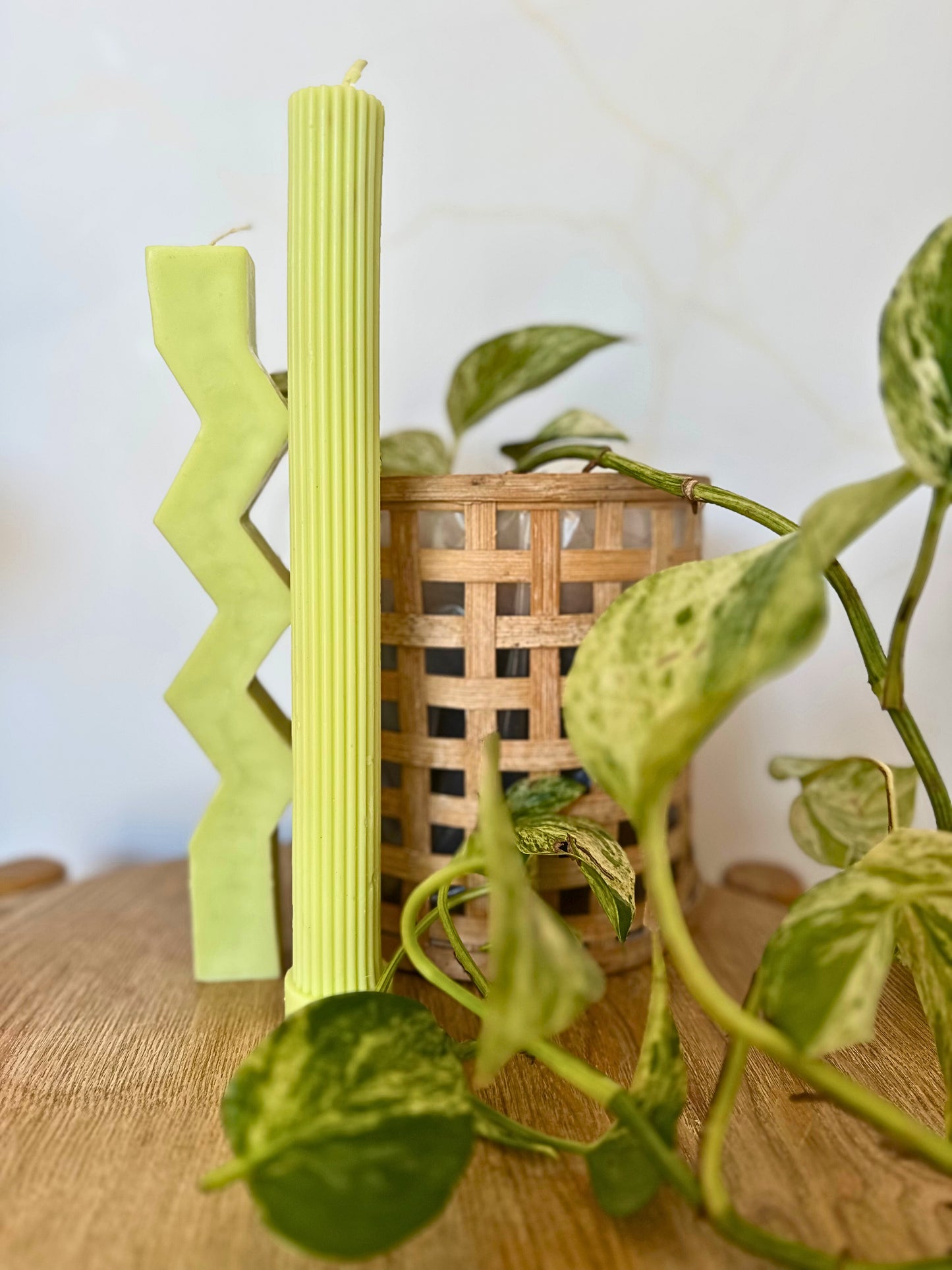 Green candlesticks with a zigzag design on a wooden surface with plants in the background