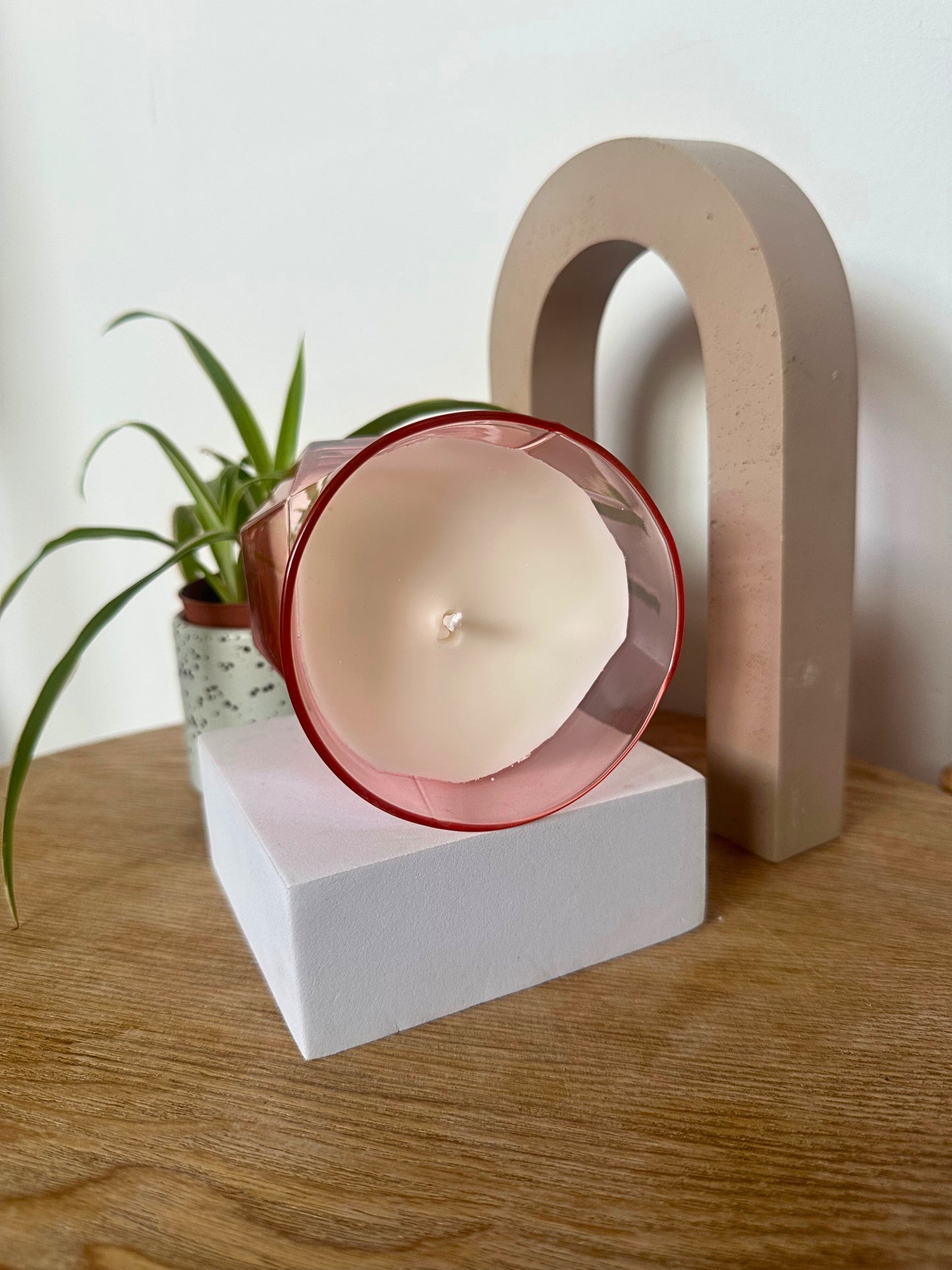 Suki Home The Pink Hikari Candle on a white block with a plant and decorative arch in the background.