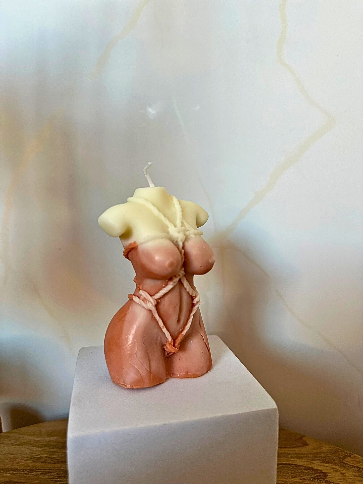Candle shaped like a female torso on a white pedestal with a light background