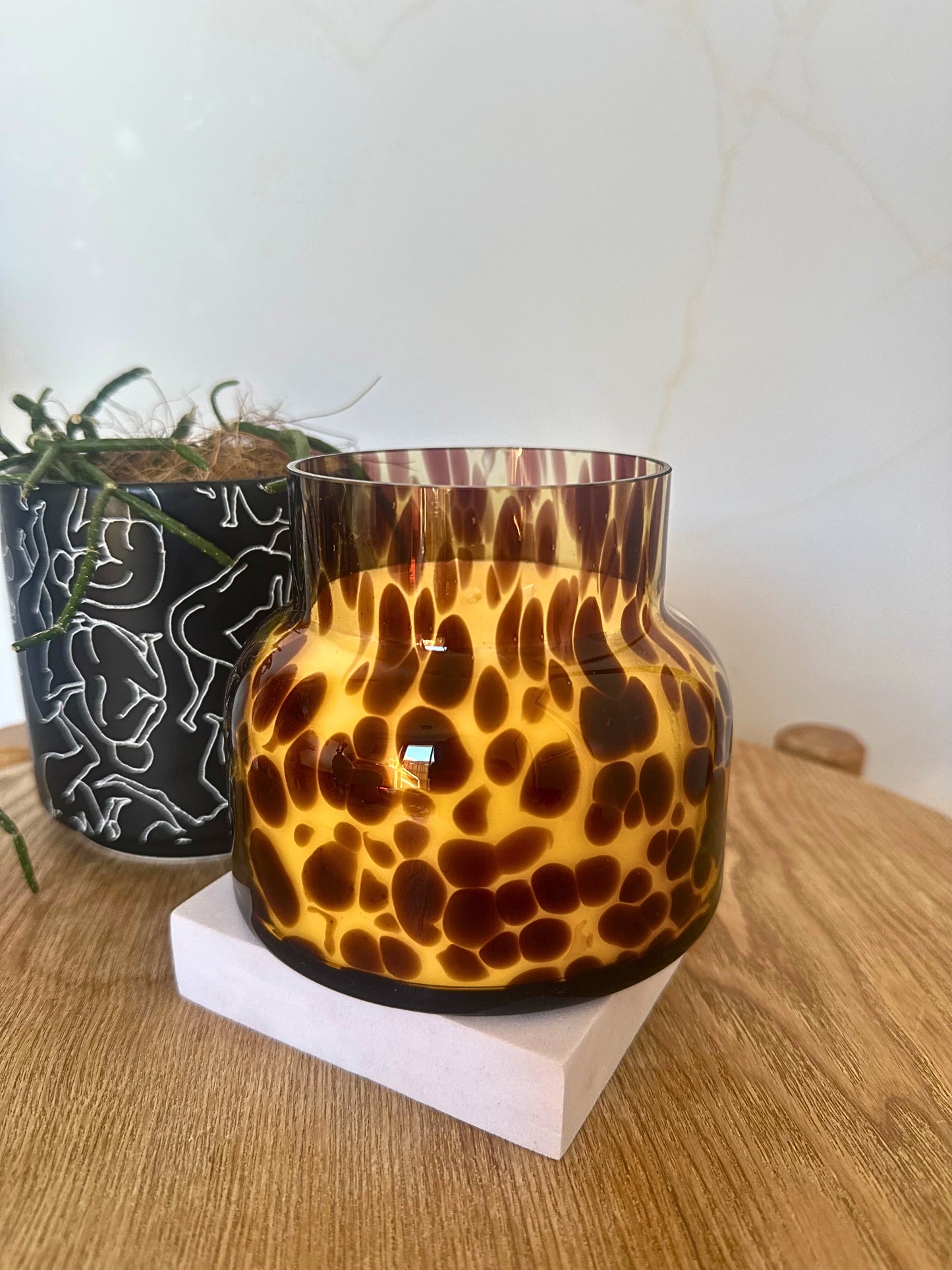 Tortoiseshell patterned candle holder on a wooden surface with a plant in the background