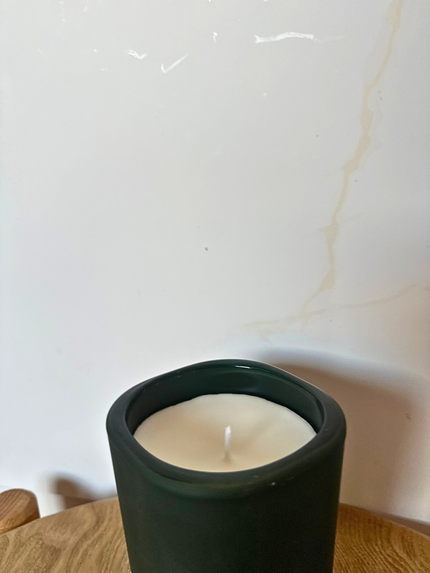 Candle in a dark green holder on a wooden surface with a white background