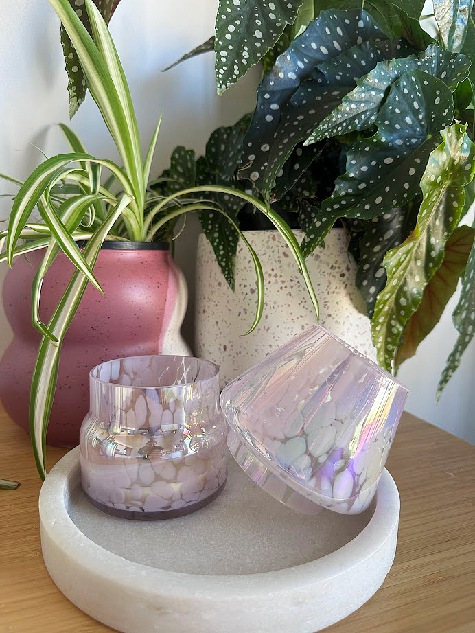 Decorative items including The Mini Mushroom Candle Lamp in Pink, on a marble stand with plants in the background.