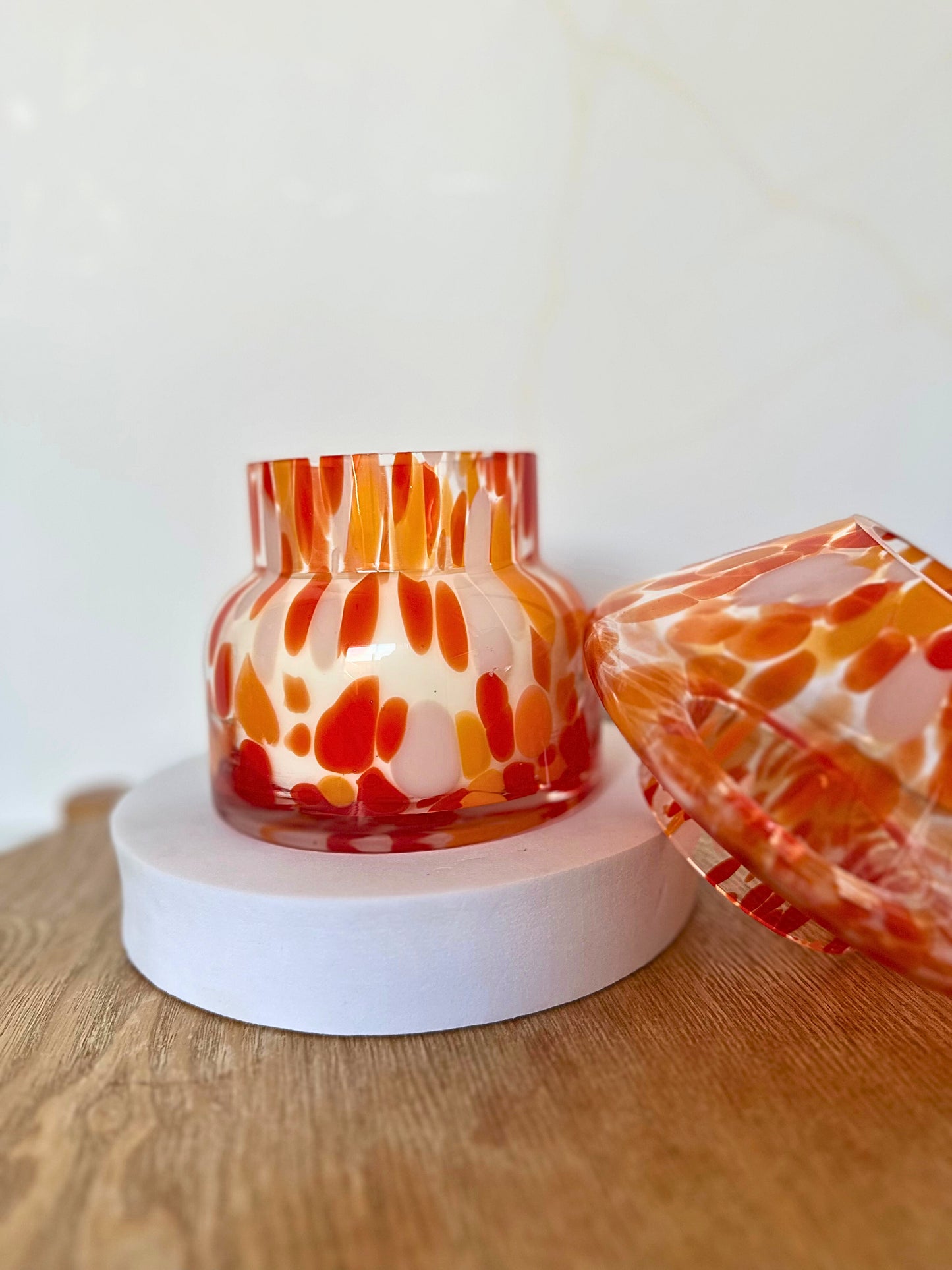 Decorative glass vase with orange and red abstract pattern on a wooden surface.