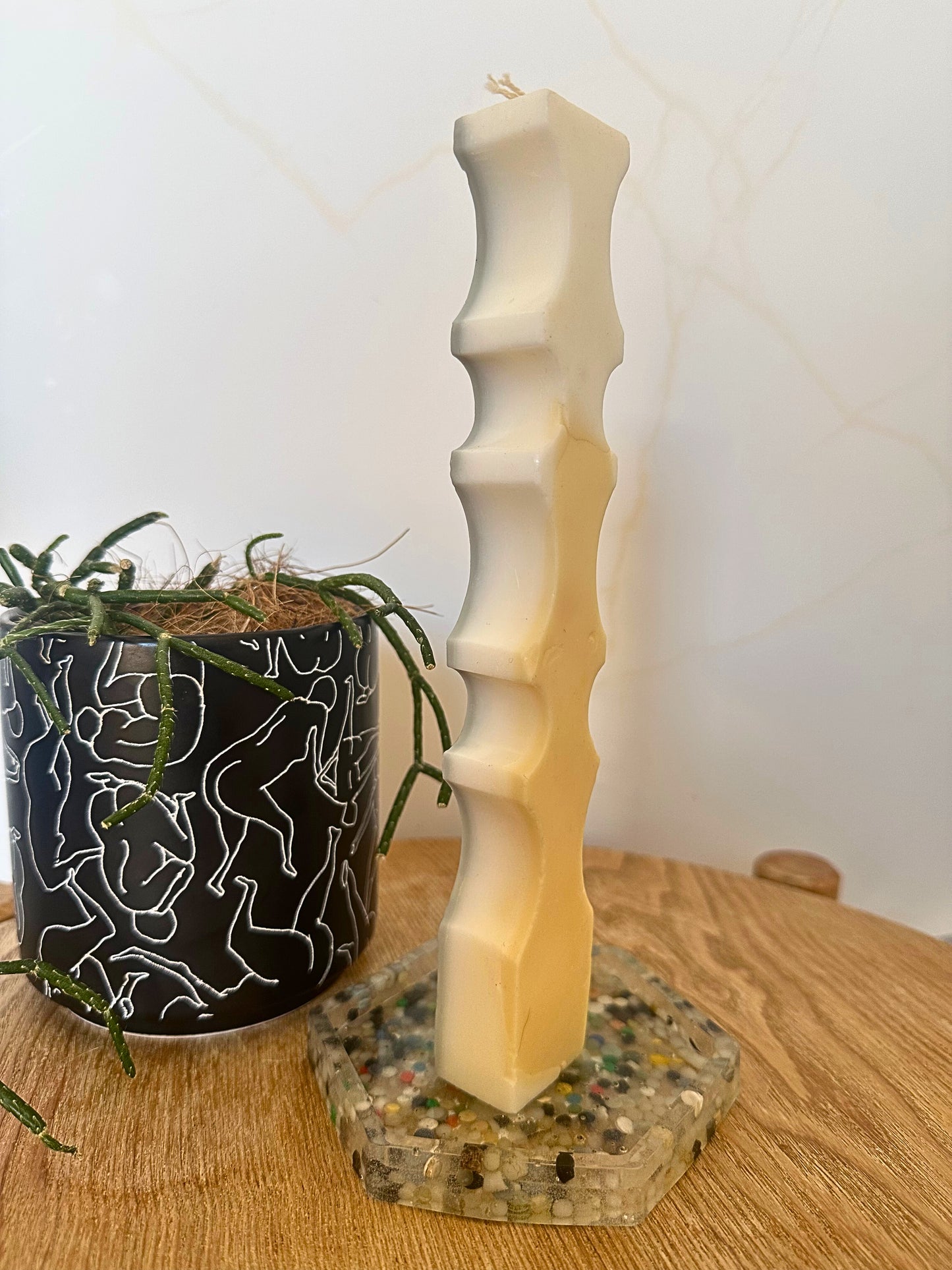 Decorative candle on a stand with a plant and patterned pot in the background