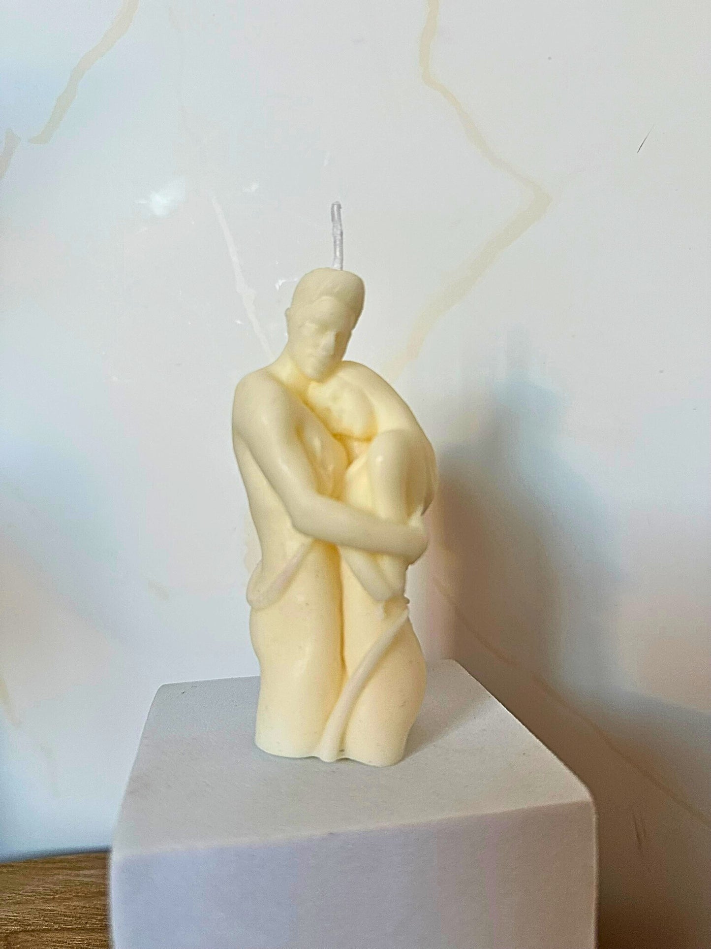 Candle shaped like a couple embracing on a white pedestal with a light background
