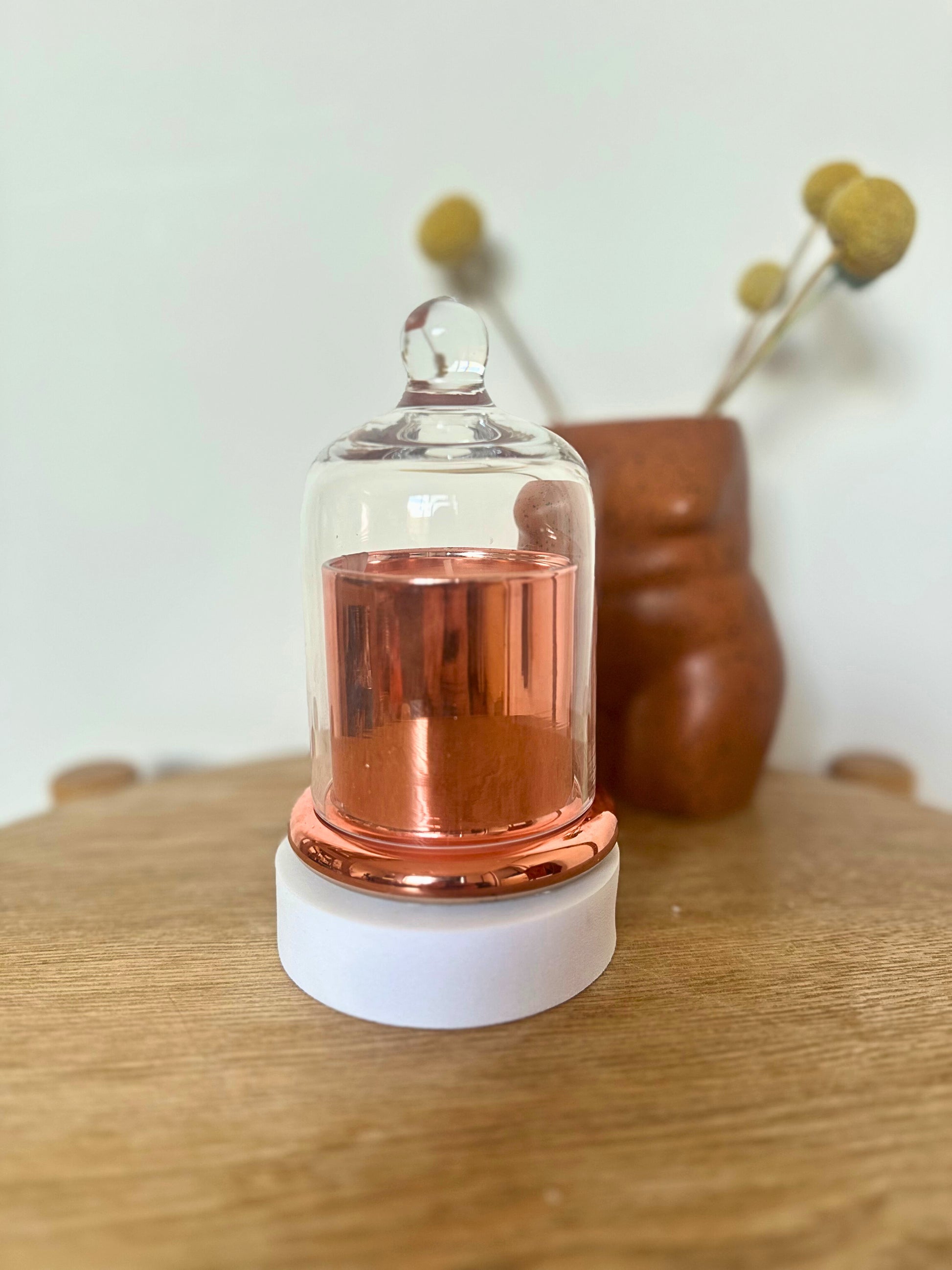 Suki Home The Seina Cloche Candle in Gold, placed on a wooden surface with a blurred background.