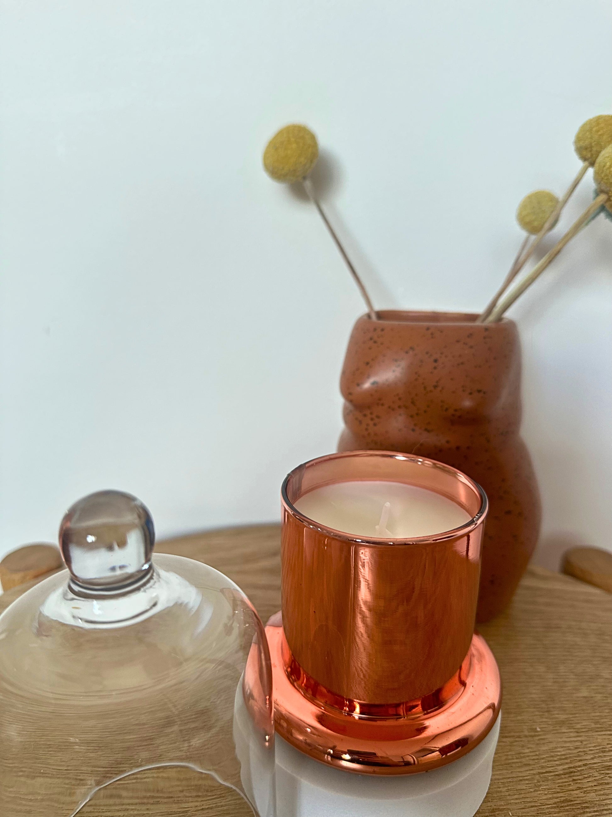 Suki Home The Seina Cloche Candle in Small Gold with a terracotta vase and dried flowers on a wooden surface.