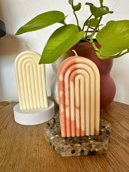 Two arch-shaped candles on decorative stands with a plant in the background.