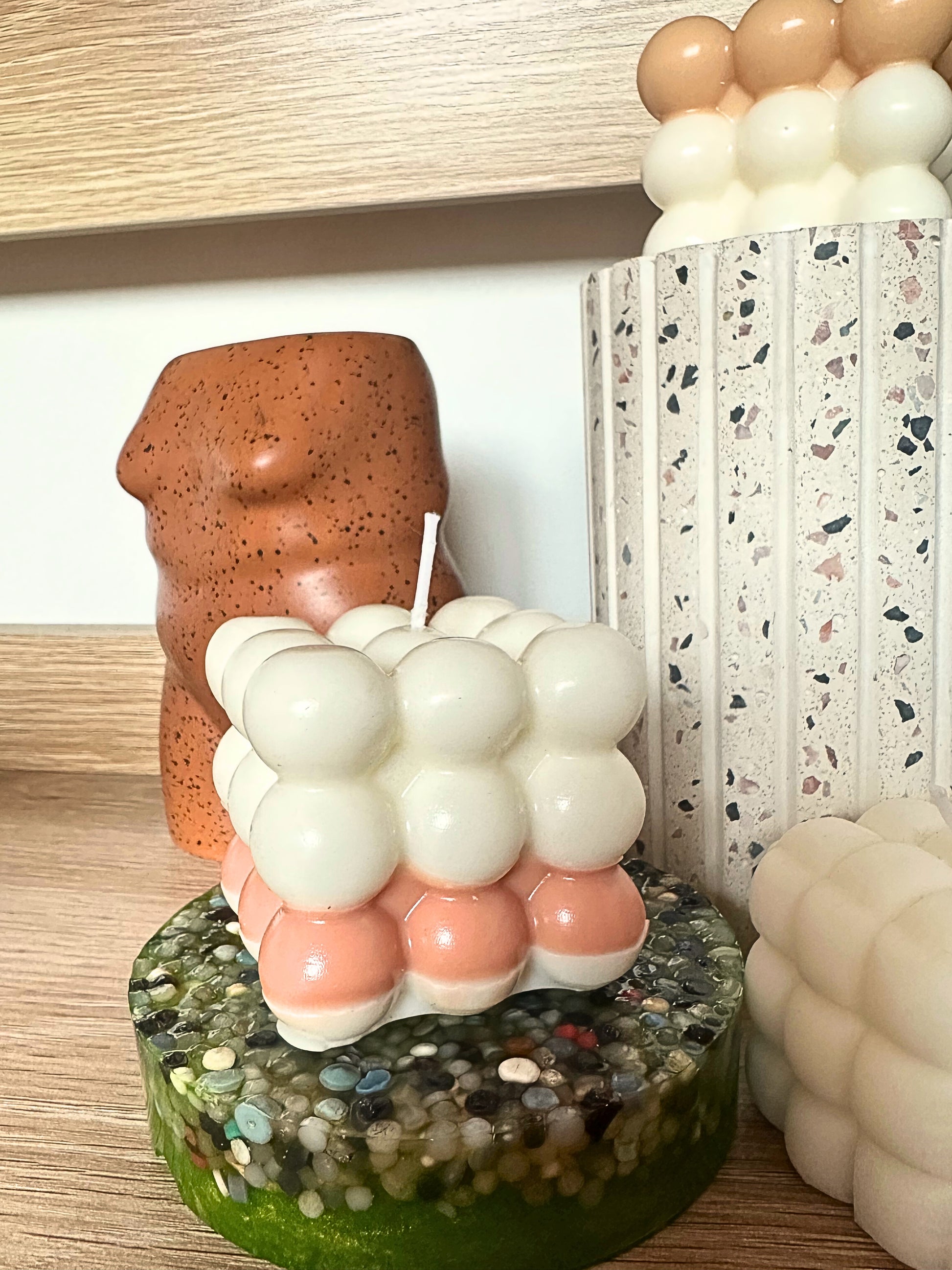 Cylindrical candle with bubble design on a textured base, surrounded by balloons.