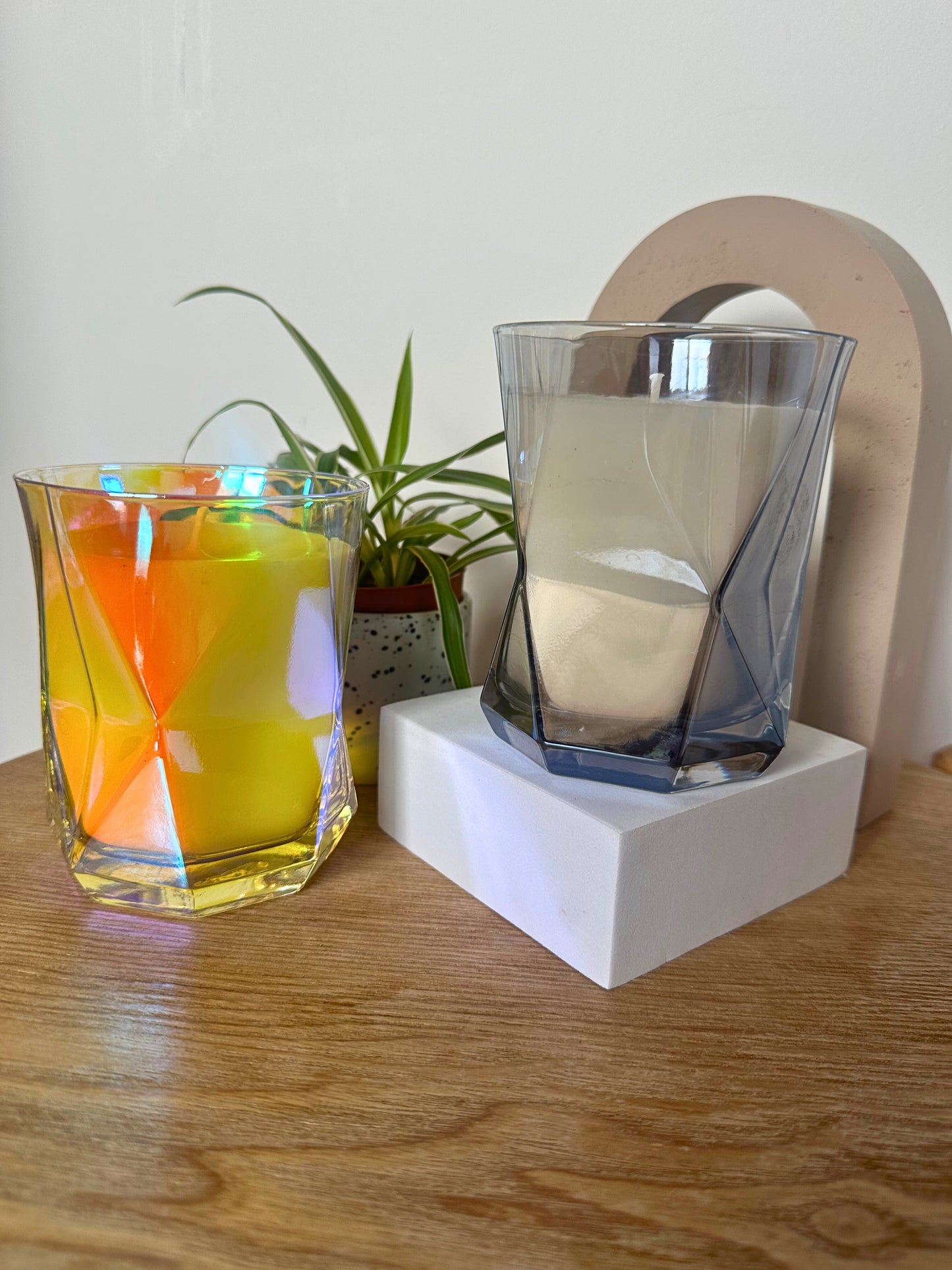 Suki Home The Hikari Candle in Crystal and in Grey on a wooden surface with a plant in the background