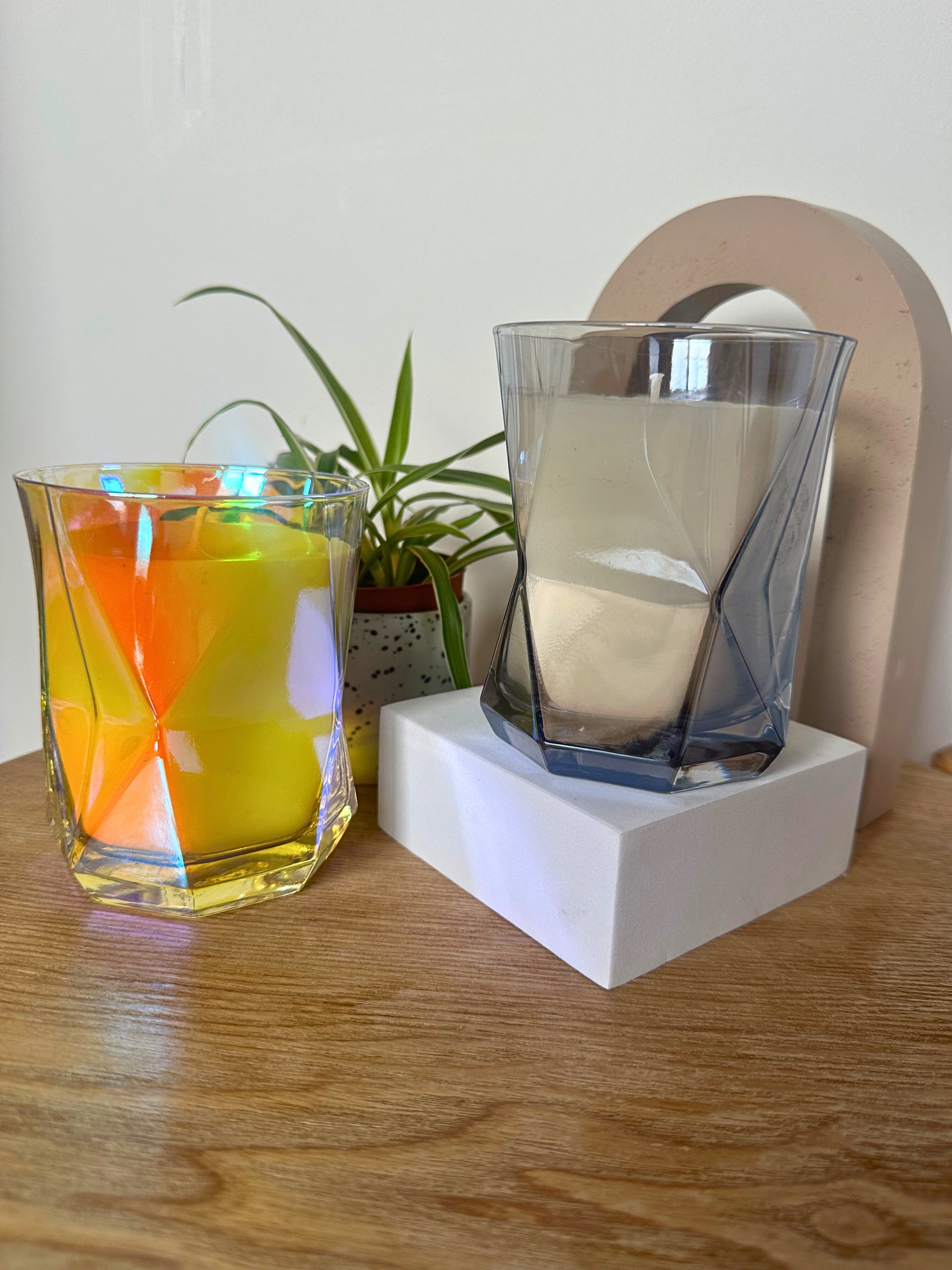Suki Home The Hikari Candle in Crystal and in Grey on a wooden surface with a plant in the background