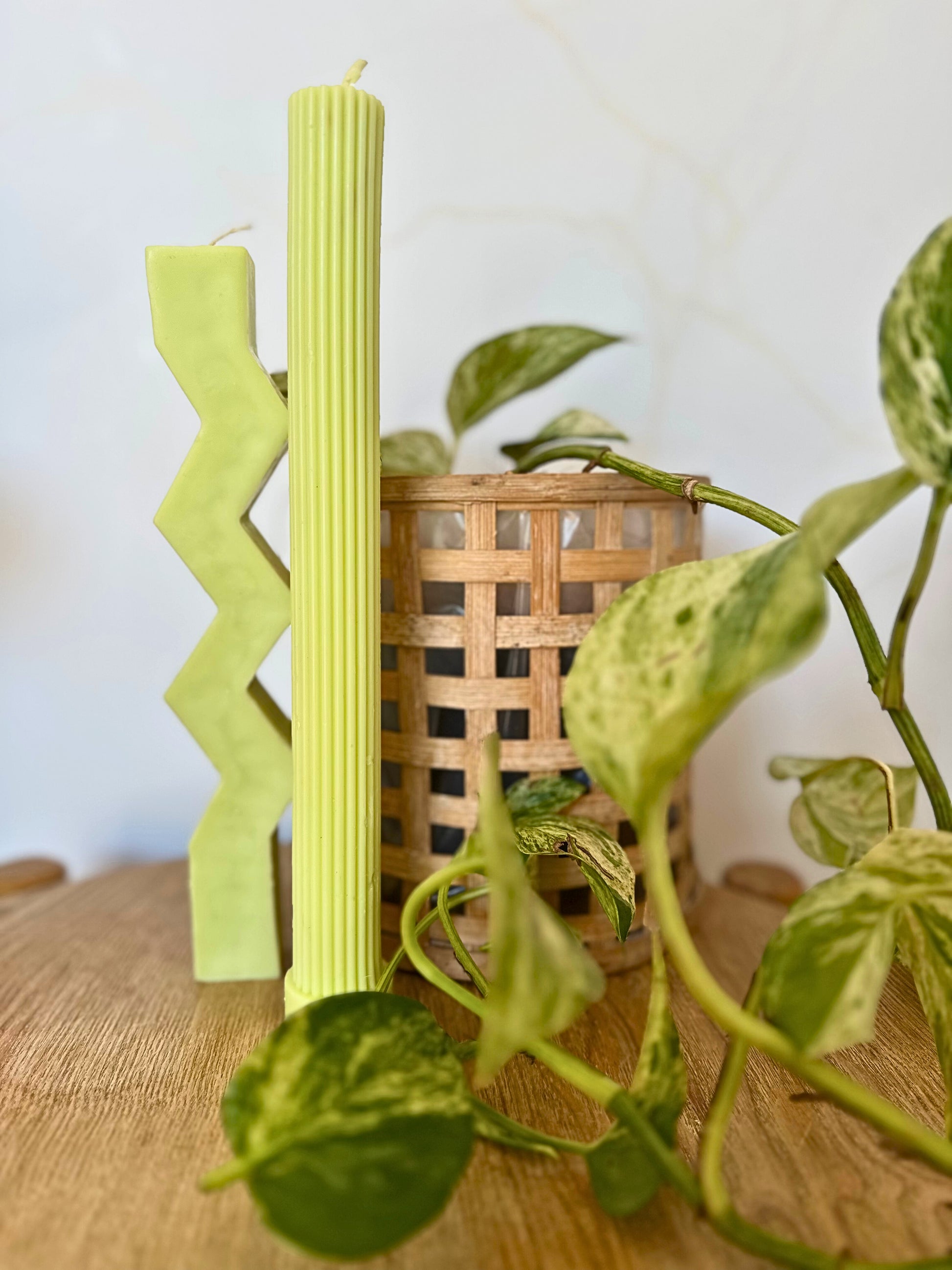 Green candlesticks with a zigzag design on a wooden surface with plants in the background