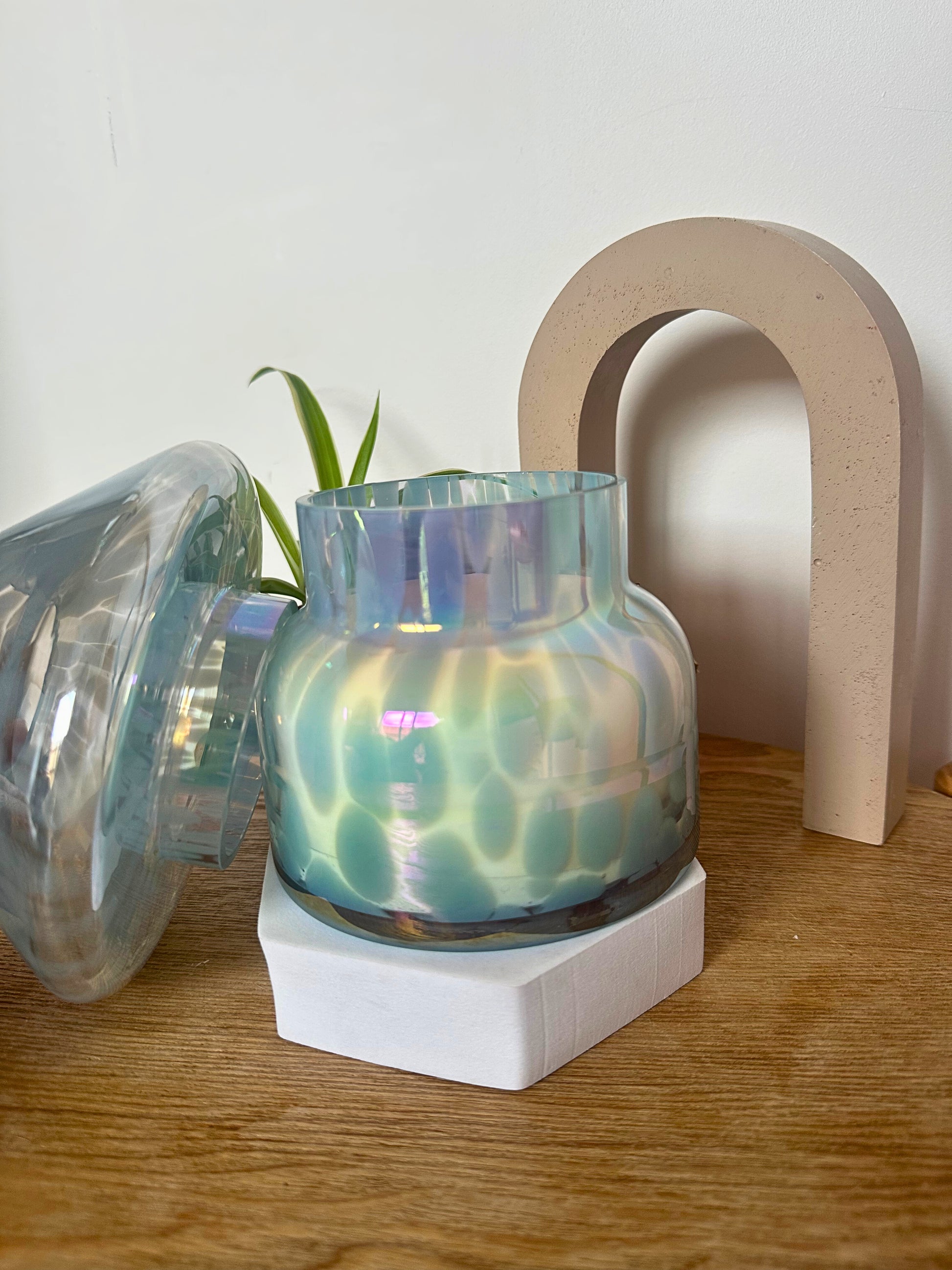 Iridescent mushroom candle lamp on a wooden surface with a white arch in the background