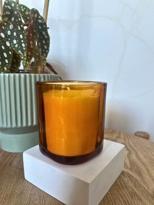Amber glass candle on a white block with a plant in the background