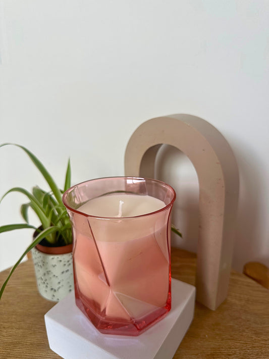 The Pink Hikari Candle on a white pedestal with a plant and decorative arch in the background
