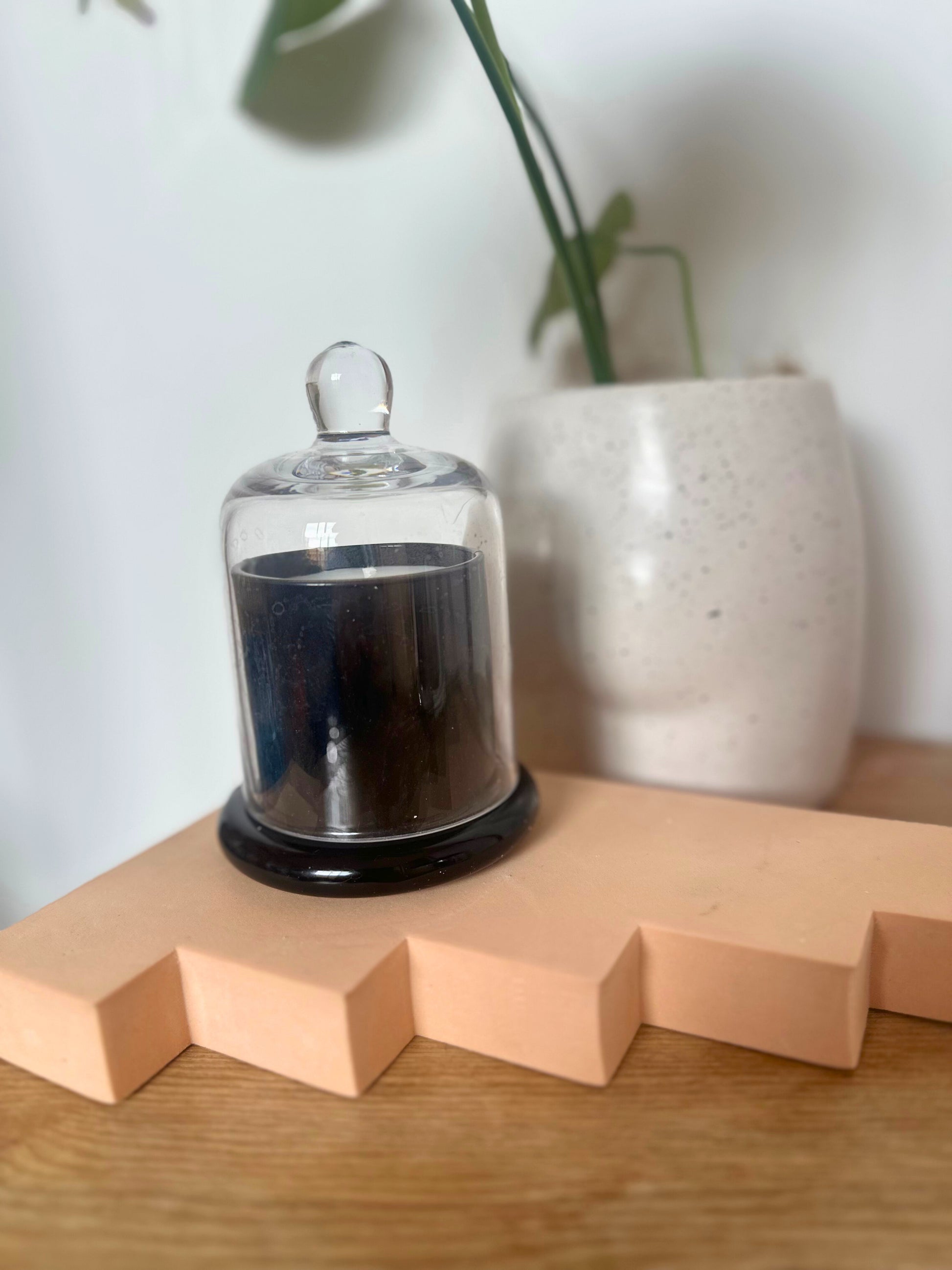 Suki Home The Seina Cloche Candle in Black on a wooden surface with a white vase in the background