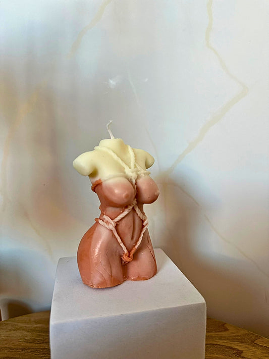 Candle shaped like a female torso on a white pedestal with a light background