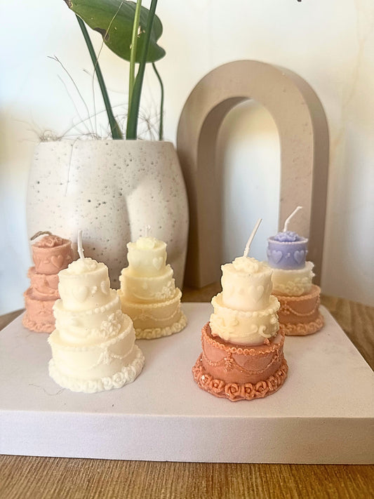 Small cake-shaped candles on a white surface with a decorative arch and plant in the background.