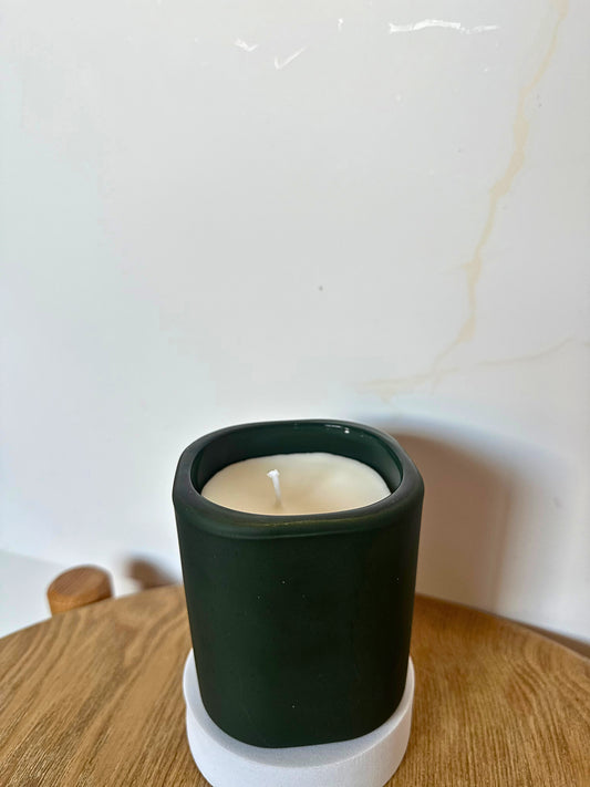 Candle in a dark green holder on a wooden surface with a white background