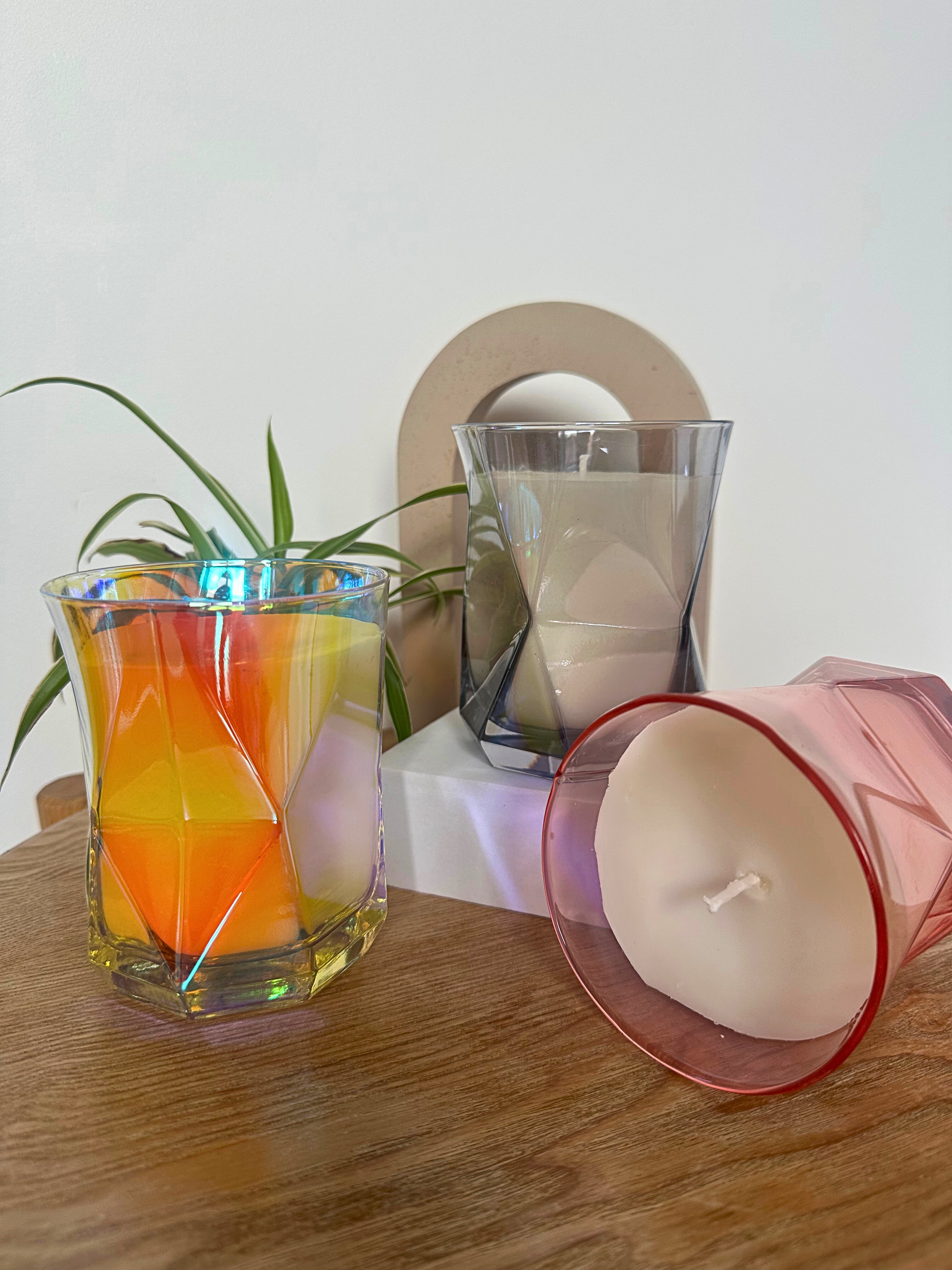 The Hikari Candle Collection in different colours on a wooden surface with a plant in the background.