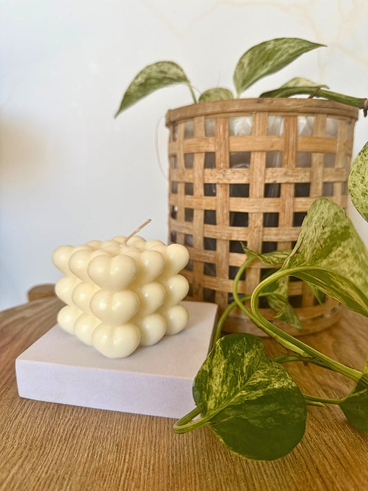 Cubical candle on a white block with a wicker basket and green leaves in the background