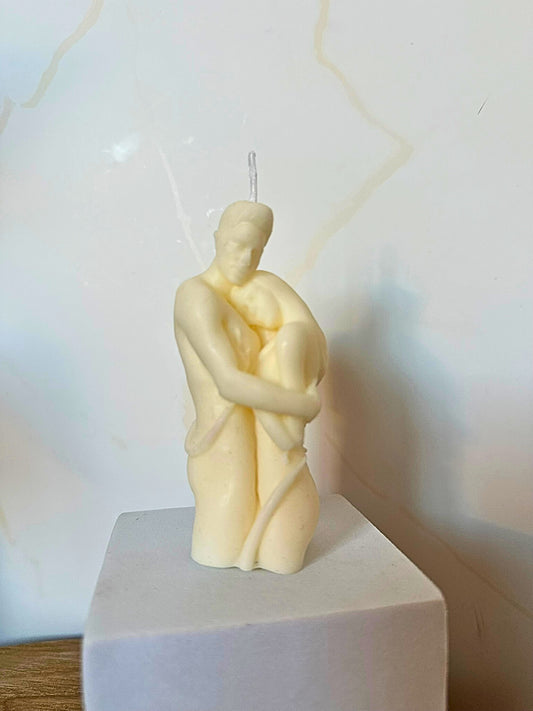Candle shaped like a couple embracing on a white pedestal with a light background